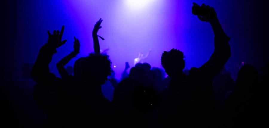 Silhouettes des invités, bras levés, sous les projecteurs bleus